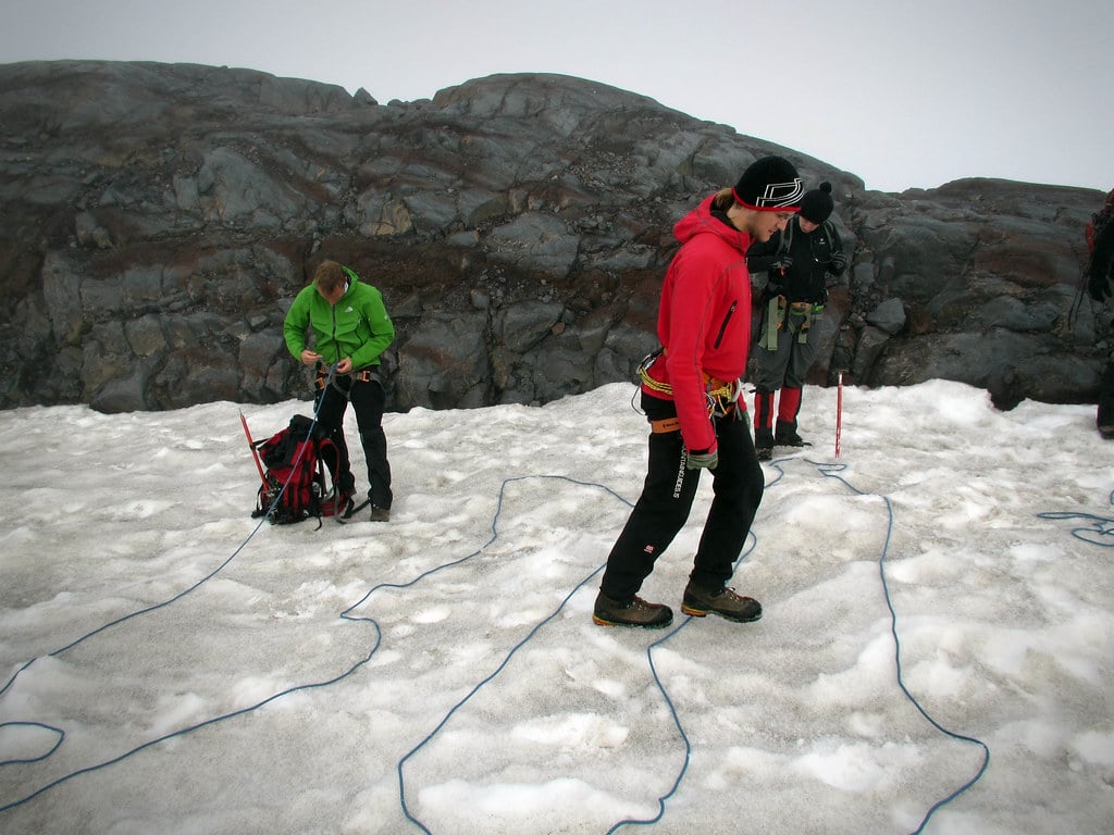 multiple people assessing their ice climbing protection gear while standing on a snowy mountain