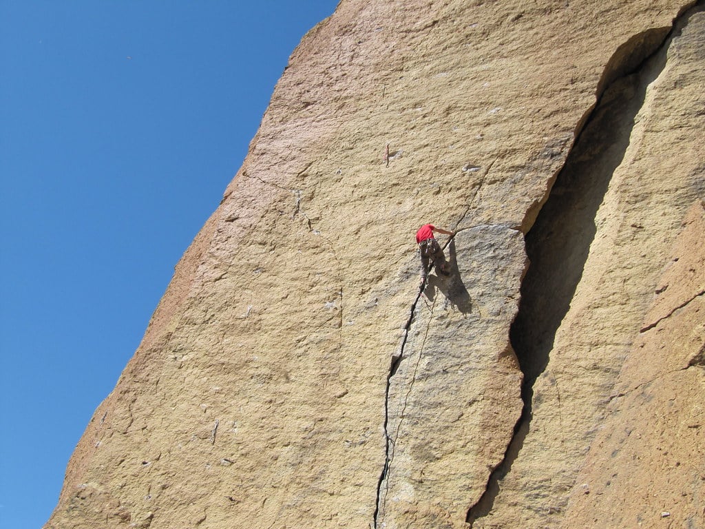 man ascending the rock face of a trad climbing routes