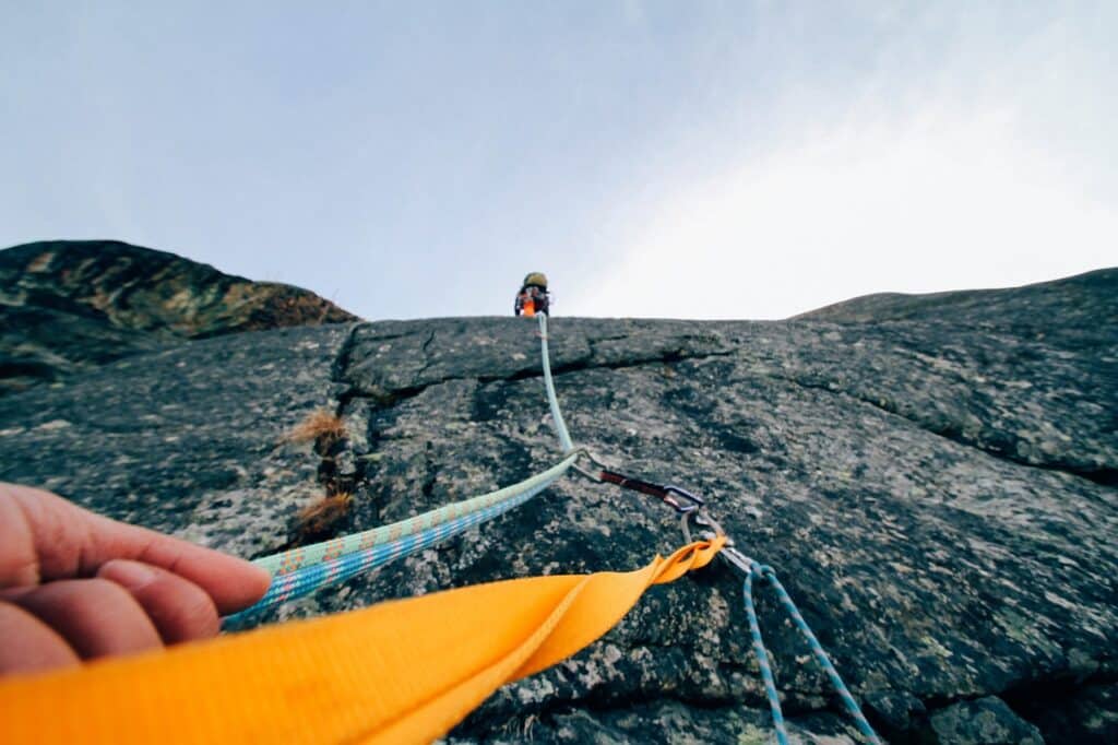 close up of a man climbing a rock face showcasing trad climbing belay devices.
