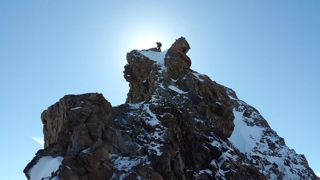 man standing at the peak of a snowy mountain using ice climbing protection