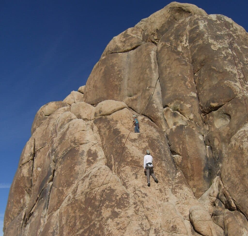 daytime photo of a parent and their child climbing a rock formation found in Joshua Tree National Park. Joshua Tree rock climbing