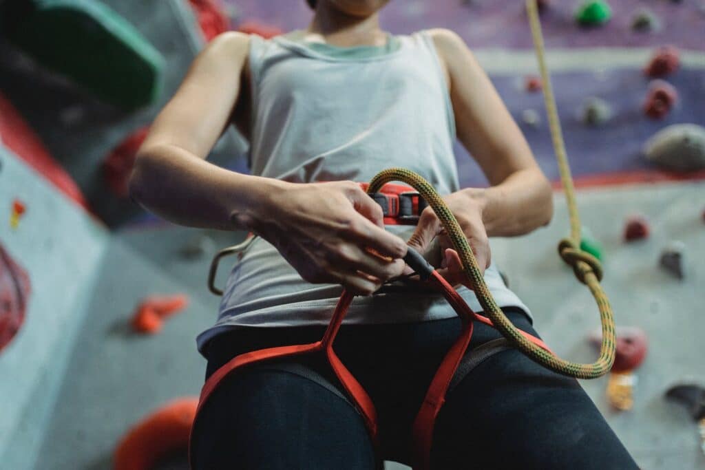 From below of crop anonymous female climber putting on cable of belay during preparation for climbing training
