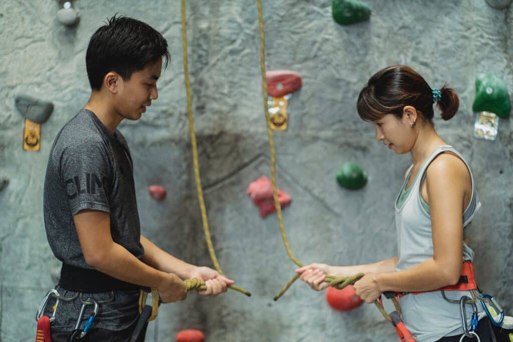 two people standing in front of an indoor rock wall communicating about rock climbing techniques. Covered in the Multi Pitch Climbing Training.