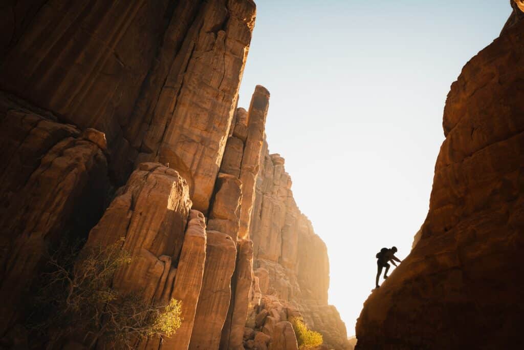 daytime landscape photo of a man scaling a rock formation detailed in the history of rock climbing article.
