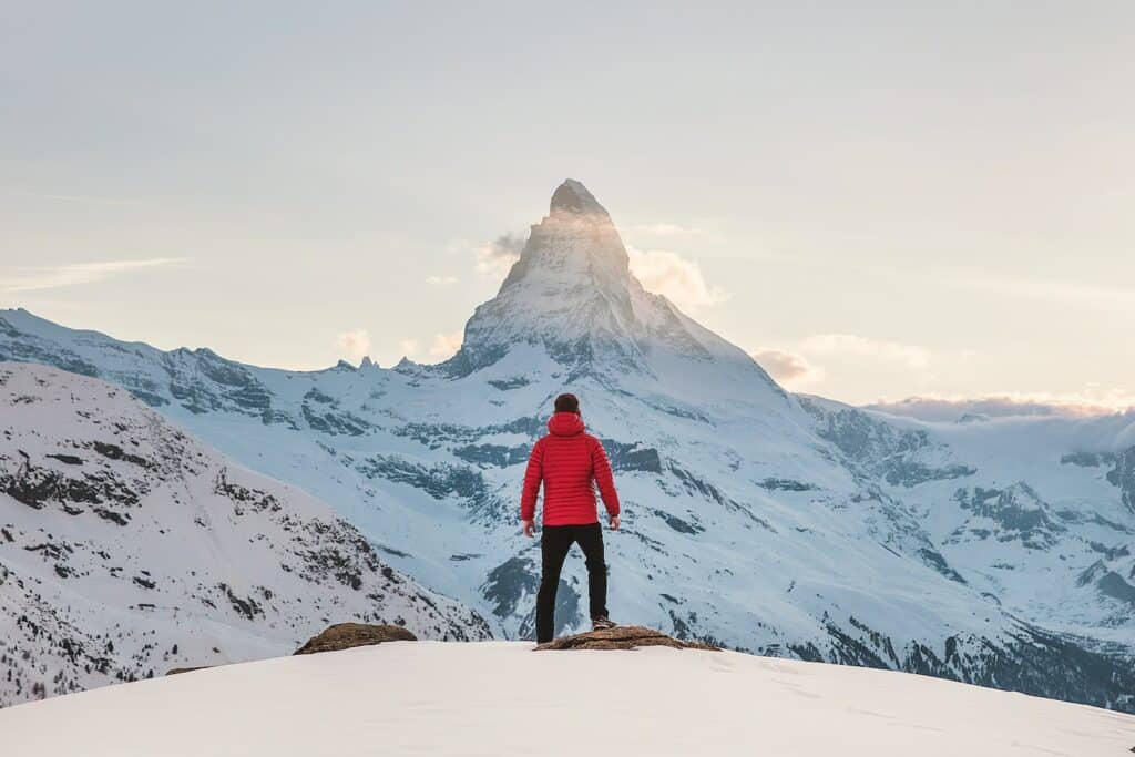 person in red snow jacket standing in front of the Matterhorn as covered in the Pro rock climber interview article.