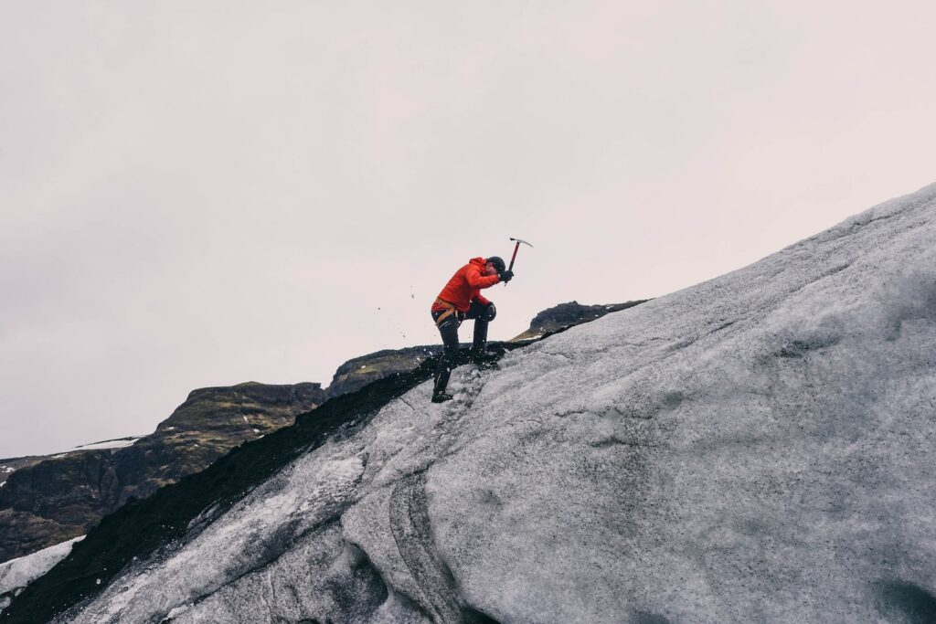 photo of a man on top of a rock formation, utilizing a pick. ice climbing for beginners article