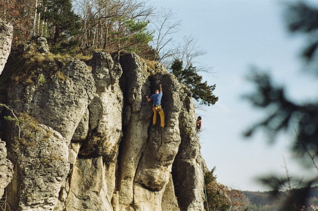 wide shot photo of man scaling the famous lime stone formations found at Frankenjura, Germany. Covered in sport climbing destinations article