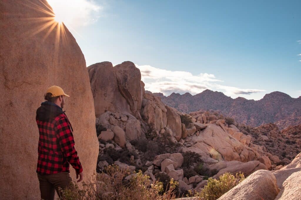 photo of a man standing next to a rock formation with a landscape view of Joshua Tree National Park. Joshua Tree rock climbing