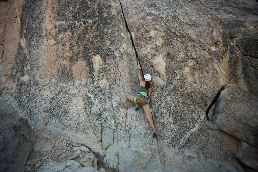 woman scaling a rock face using trad climbing offwidth techniques