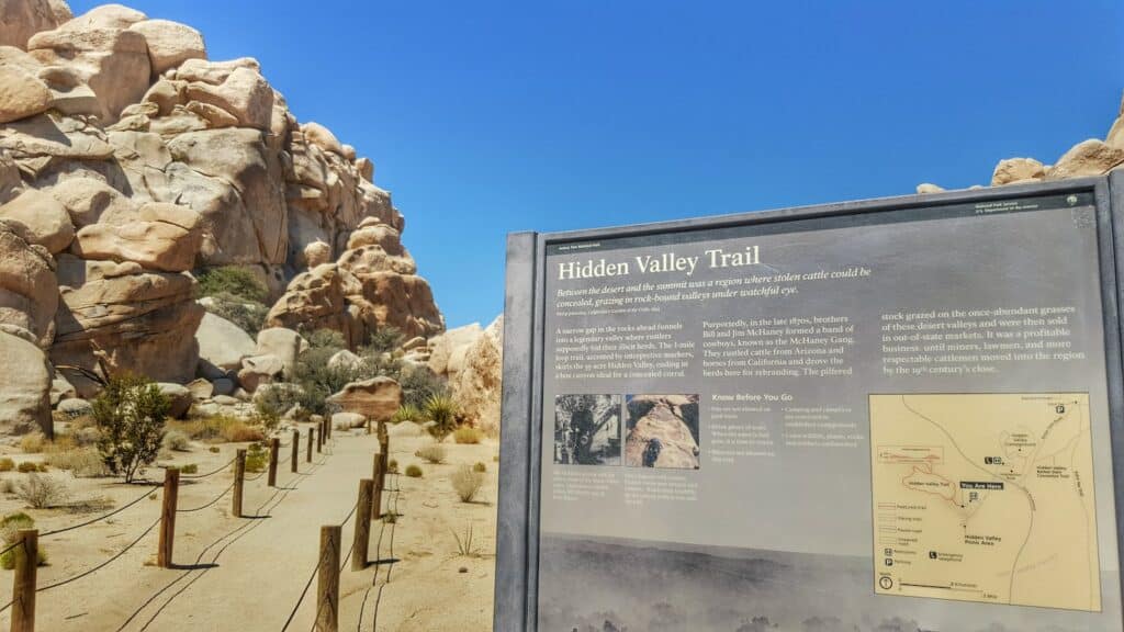 close up photo of Hidden Valley Trail informational plaque with large rock formations in the back ground. encapsulating the theme of the article best campsites in Joshua Tree.