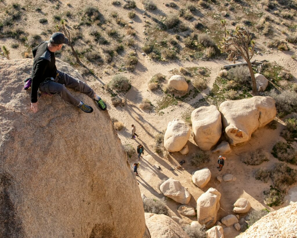 a man sitting on top of a large rock found on a joshua tree climbing routes