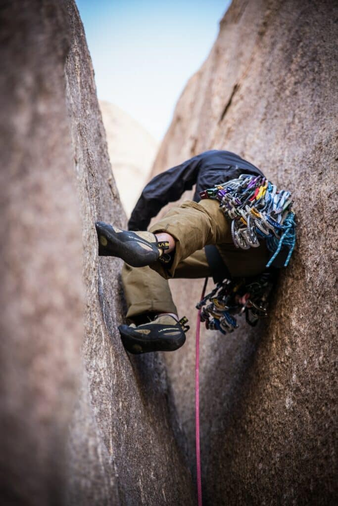 Man expertly navigating a challenging rock climb wedged between two massive rock formations, with a close-up on his durable and flexible climbing pants, showcasing the high-quality gear featured in 'Best Rock Climbing Pants for Men in 2024'