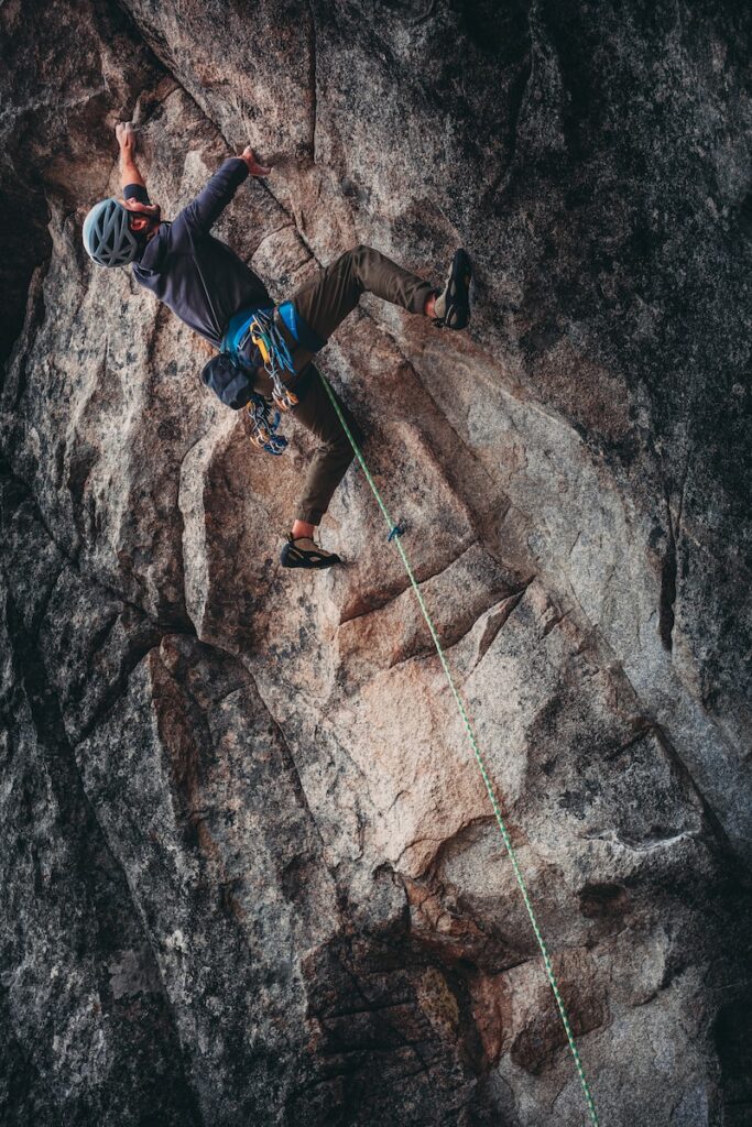 Man scaling a rock face equipped with essential climbing gear, demonstrating successful application of 'Bouldering Techniques' from the instructional article.