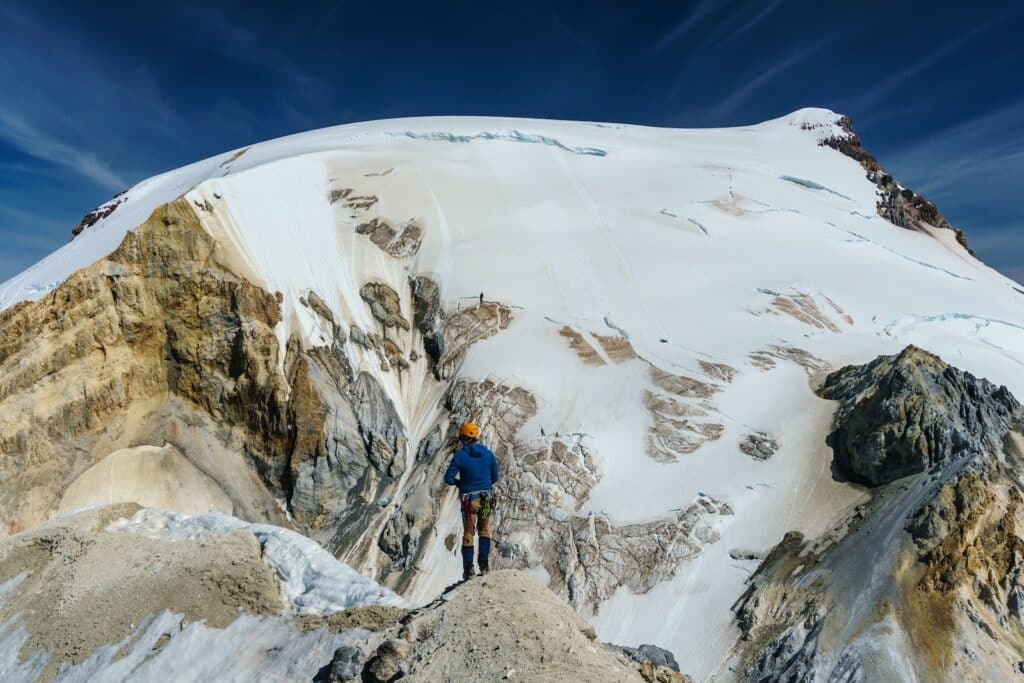 man in blue jacket and black pants standing on snow covered mountain