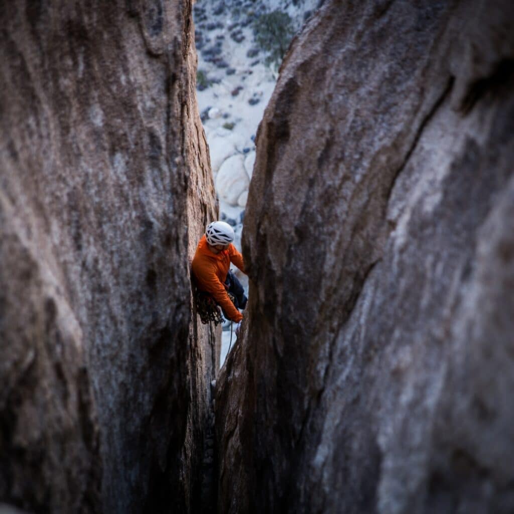 man preparing to climb rock crack while using all necessary gear for trad climbing off width