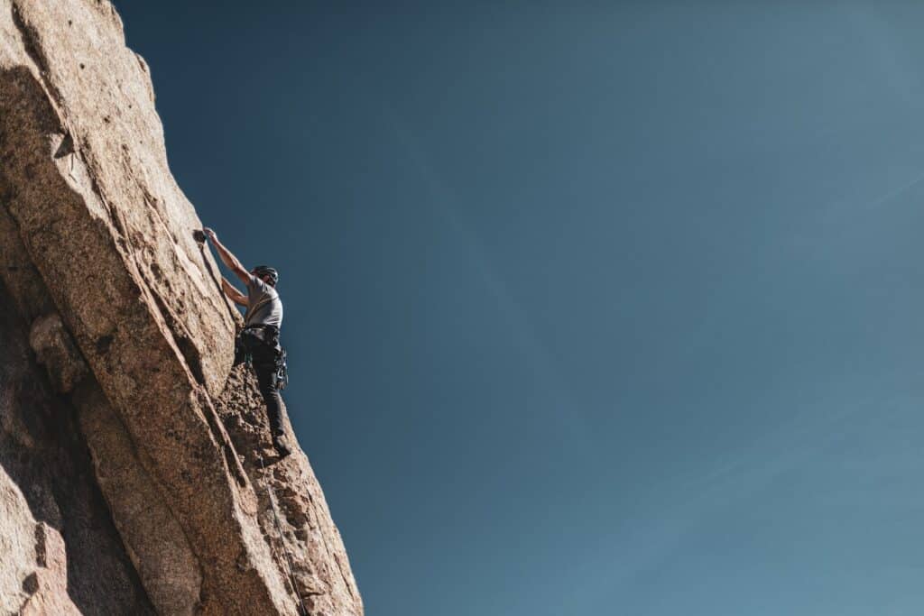 man scaling a rock wall wearing a trad climbing harnesses