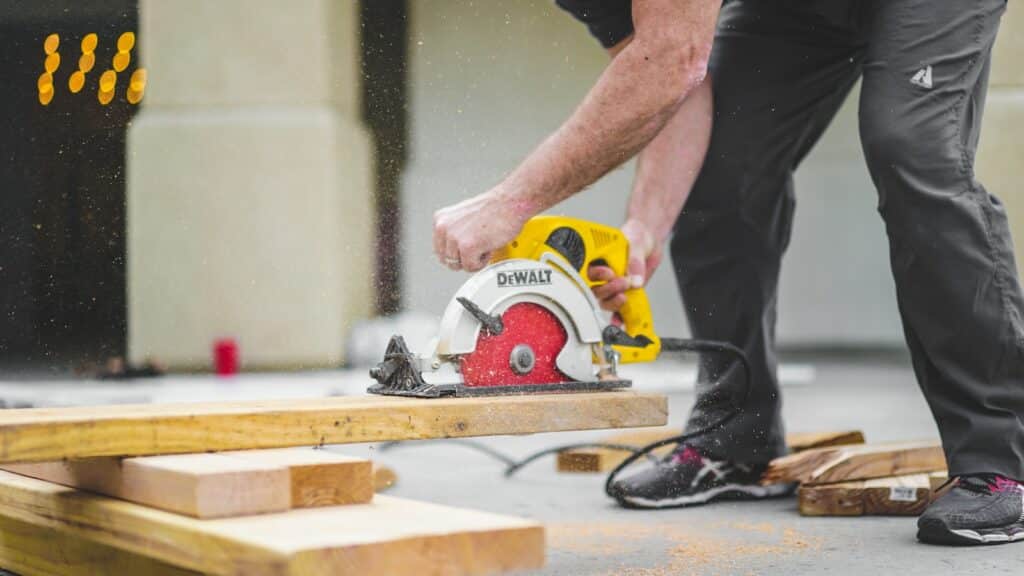 man in black sweatpants using DEWALT circular saw and cutting a wood plank to create the wood frame for a DIY Rock climbing wall