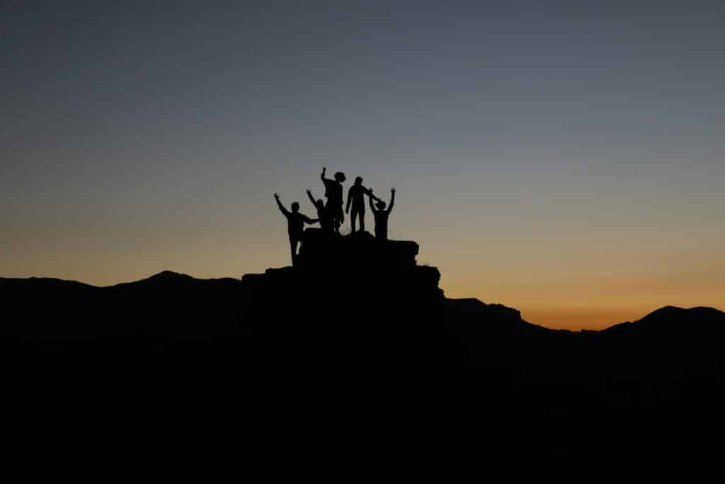 photo of 5 peoples silhouette outside while standing at the peak of a rock formation as covered in the history of rock climbing article